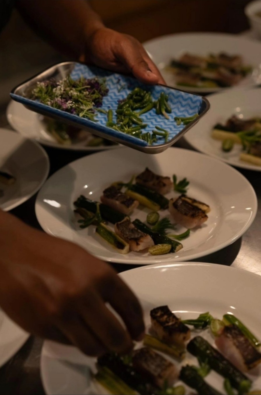 Hands carrying a tray of herb salad past plated fish
