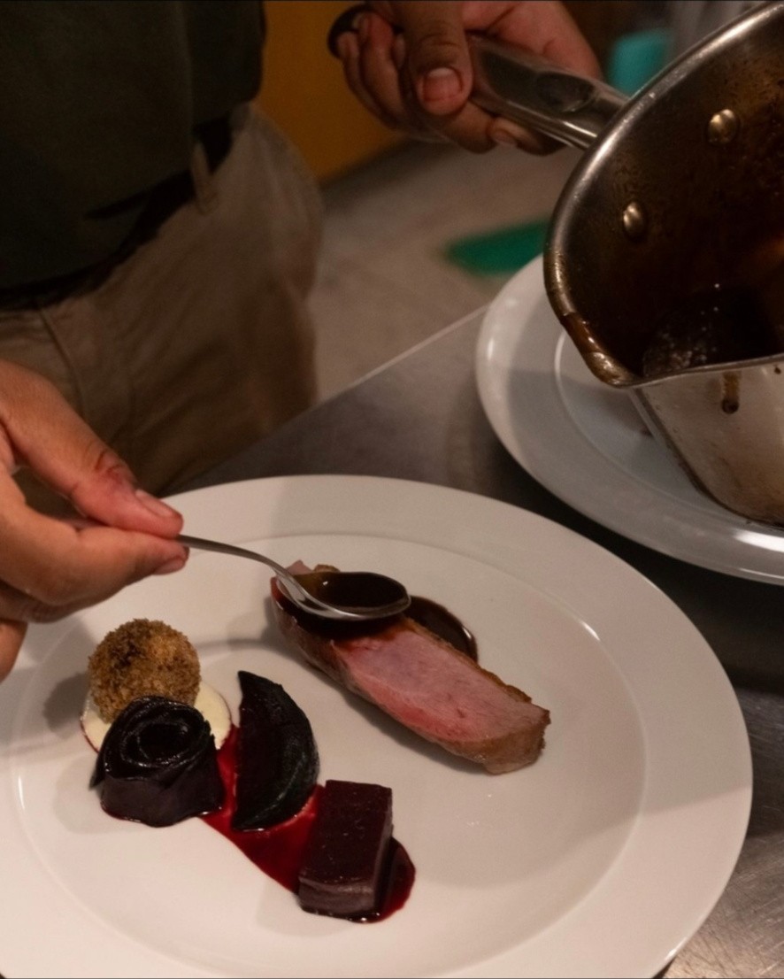 Hands spooning sauce over duck and beetroot